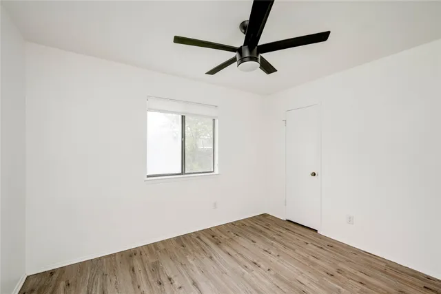 an empty room with wooden floor fan and windows