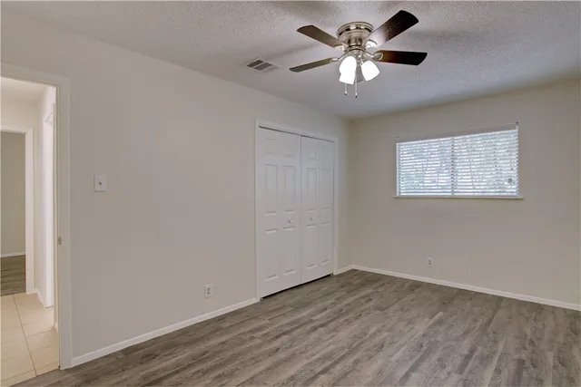 an empty room with wooden floor chandelier fan and windows