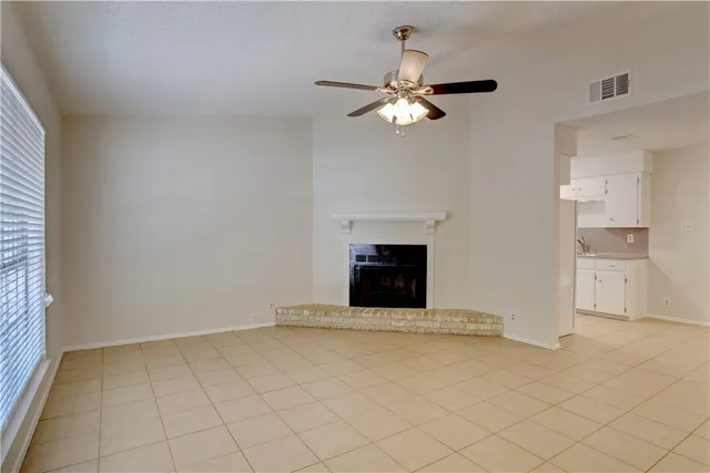 a view of an empty room with chandelier fan and fire place