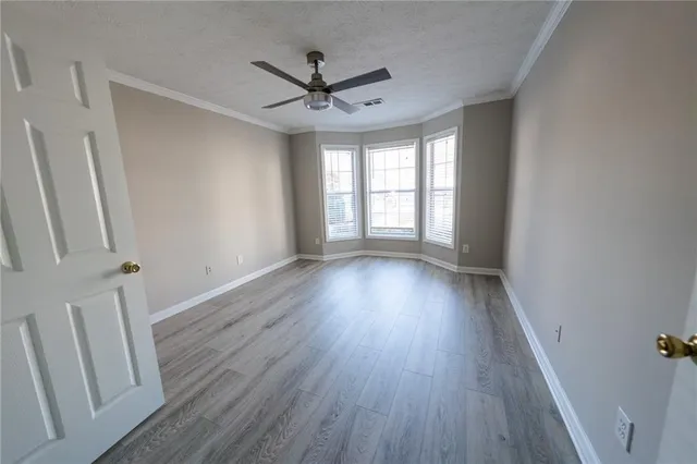 an empty room with wooden floor fan and windows