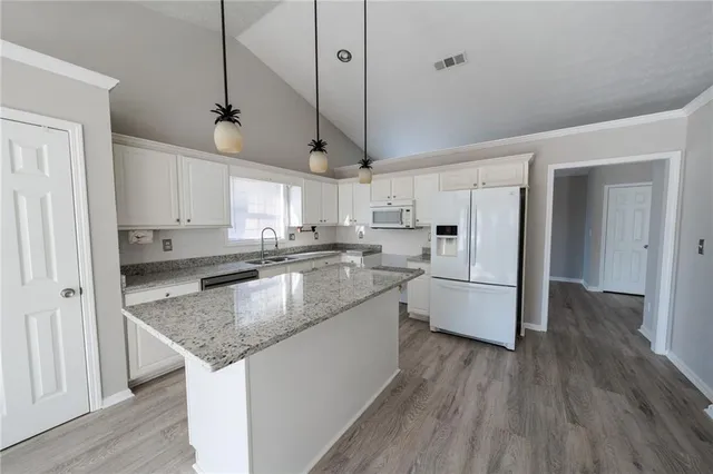 a kitchen with stainless steel appliances granite countertop a sink a refrigerator a center island and wooden floor