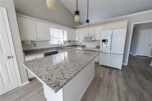 a kitchen with stainless steel appliances granite countertop a refrigerator a sink dishwasher a stove and white countertops with wooden floor