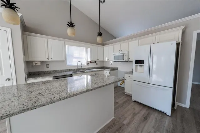 a kitchen with stainless steel appliances granite countertop a refrigerator a sink dishwasher a stove with white cabinets and wooden floor