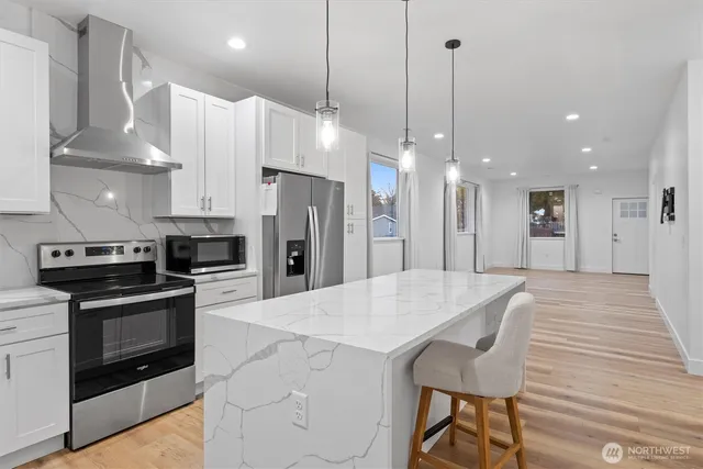 a kitchen with stainless steel appliances a stove a refrigerator a oven and white cabinets with wooden floor