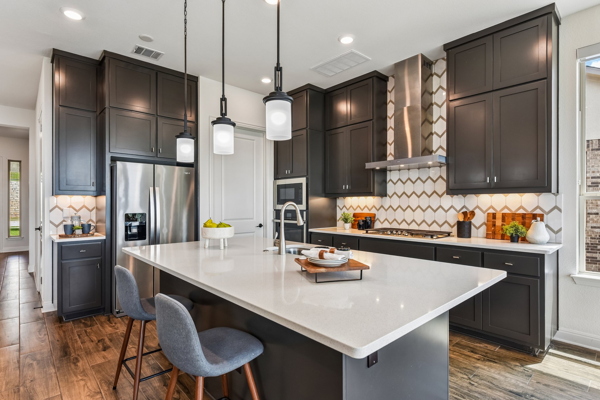 19113 Freeman Circle Austin, TX 78738 - Photo 3 of 37 Sleek, modern kitchen with rich cabinetry, a spacious island, and pendant lighting for elevated culinary experiences.