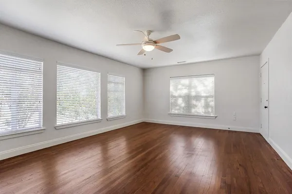 an empty room with wooden floor ceiling fan and windows