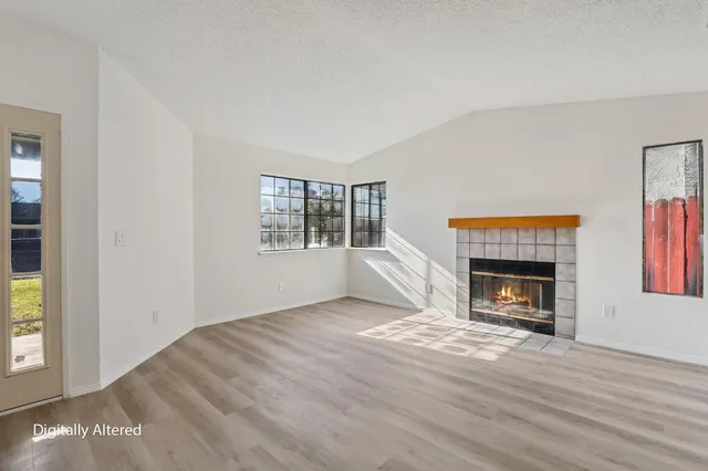 an empty room with wooden floor fireplace and windows