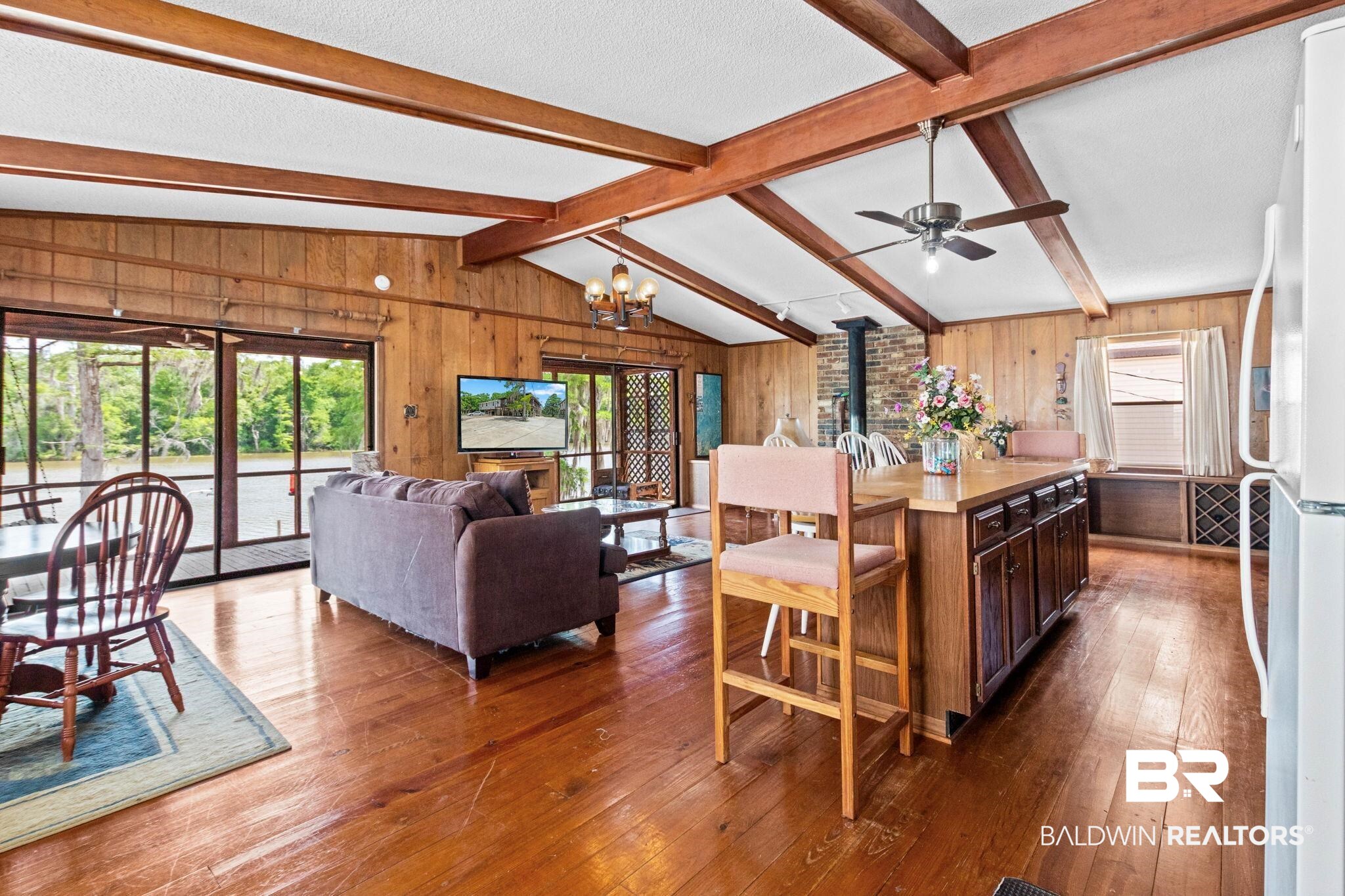 8153 Bryant's Lndg Road Stockton, AL 36579 - Photo 25 of 87 Vaulted ceiling with exposed wood beams, wood-finish flooring, wood paneling, floor-to-ceiling windows, and a central kitchen island with integrated cabinetry