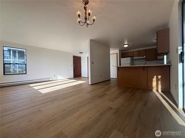 a view of empty room with wooden floor and kitchen view