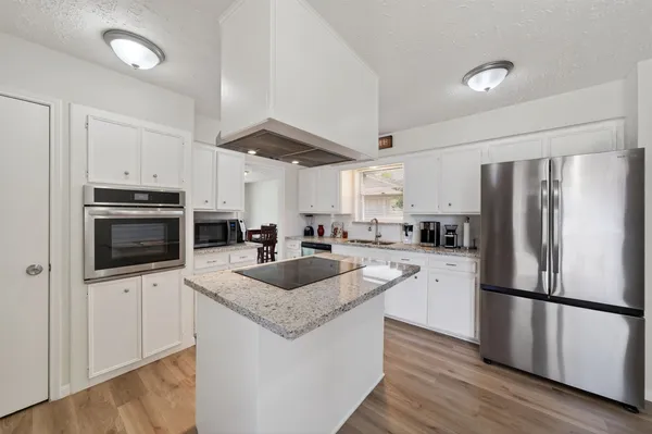 a kitchen with granite countertop a refrigerator a sink a stove a microwave and wooden floor