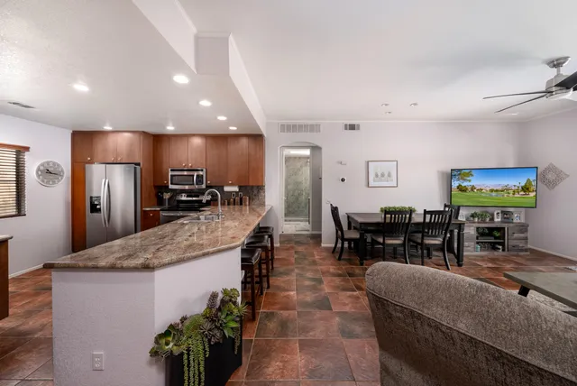 a kitchen with stainless steel appliances kitchen island granite countertop a refrigerator a sink a dining table and chairs with wooden floor