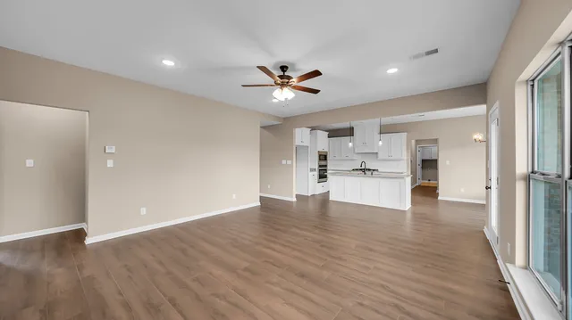 a view of an empty room and kitchen with wooden floor