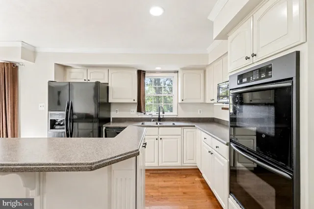 a kitchen with stainless steel appliances granite countertop a refrigerator a stove and a sink with wooden floors