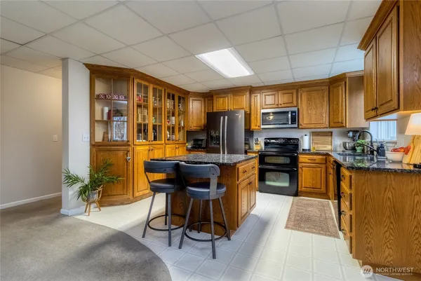 a kitchen with stainless steel appliances kitchen island granite countertop a refrigerator a stove a sink a dining table and chairs with wooden floor