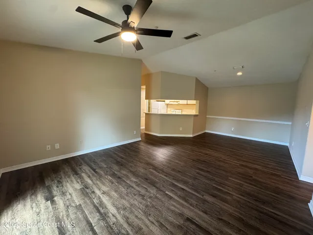 an empty room with wooden floor chandelier fan and windows