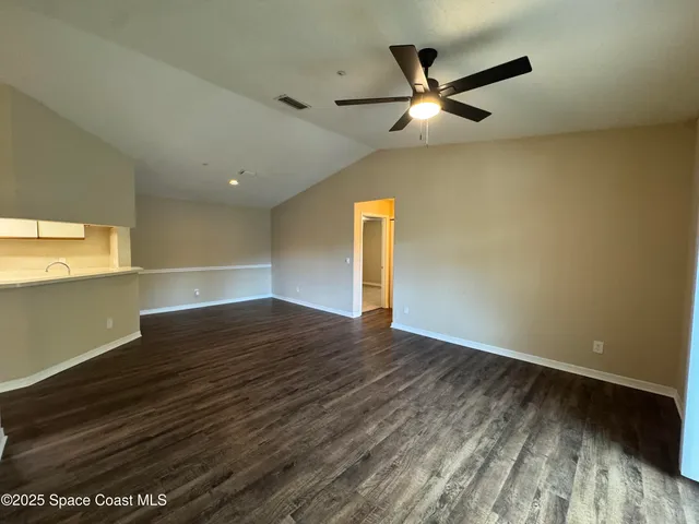 a view of an empty room with wooden floor and a ceiling fan