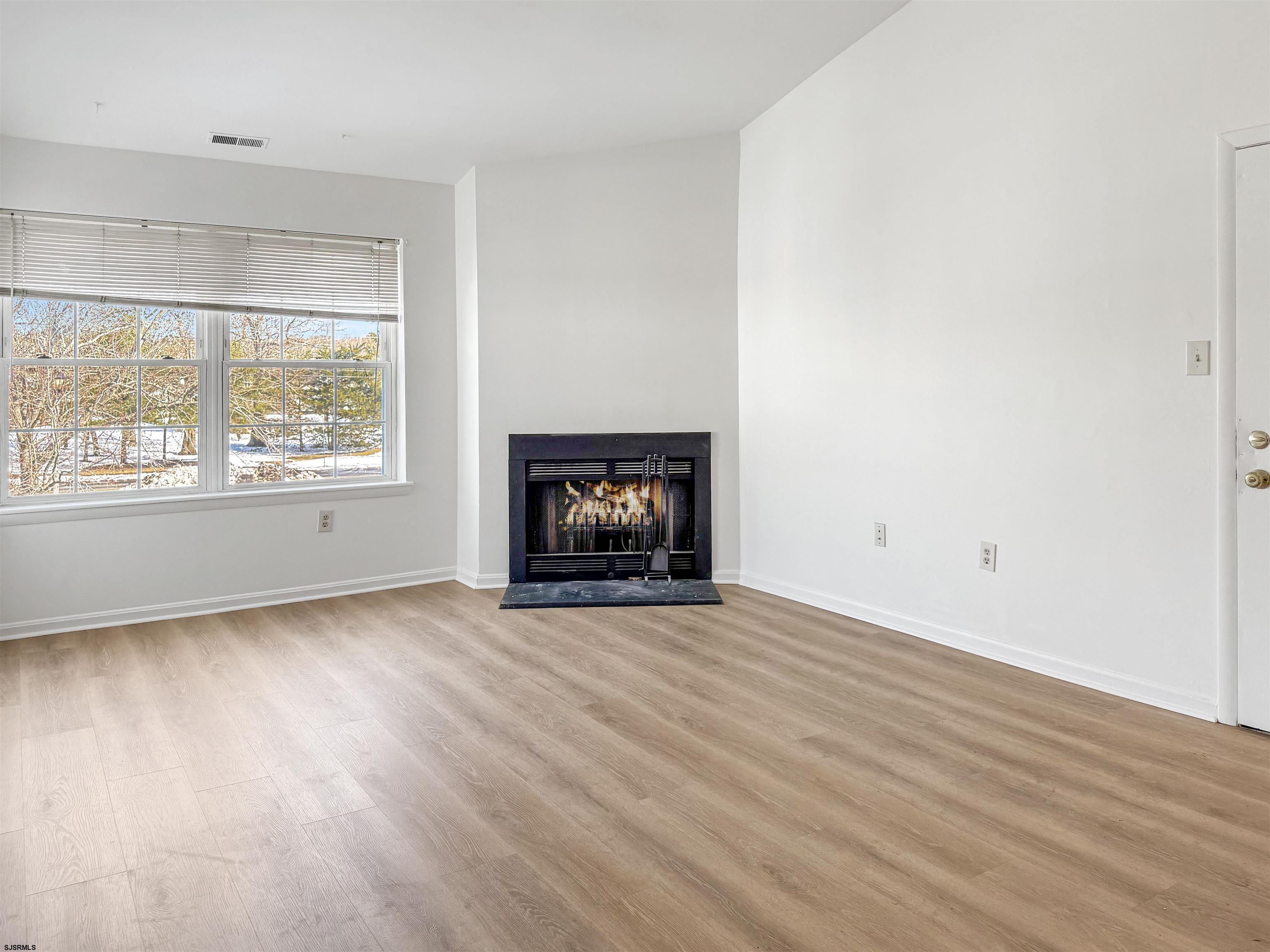 132 Meadow Ridge Road, Unit 132 Smithville, NJ 08205 - Photo 2 of 7 an empty room with wooden floor fireplace and window
