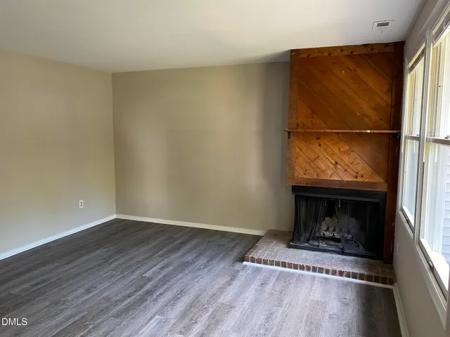 a view of an empty room with wooden floor fireplace and a window