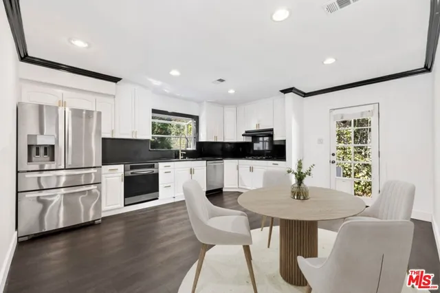 a kitchen with stainless steel appliances granite countertop a refrigerator a stove a sink a dining table and chairs with wooden floor