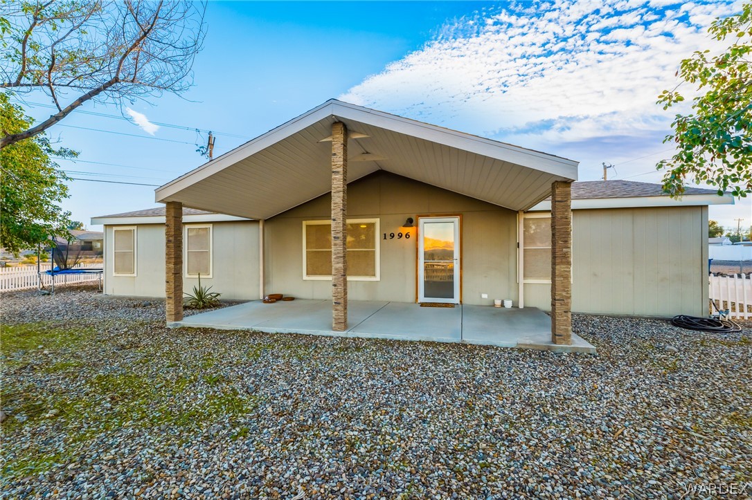 1996 Ramar Road Bullhead City, AZ 86442 - Photo 2 of 65 The property features a covered front porch supported by two stone-clad pillars, a light-colored exterior, and an entry door with a full-view glass panel