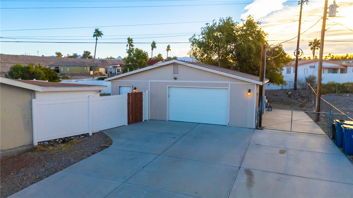 1996 Ramar Road Bullhead City, AZ 86442 - Photo 41 of 65 The property features a garage with a white door, a paved driveway, and a white fence with a wooden gate