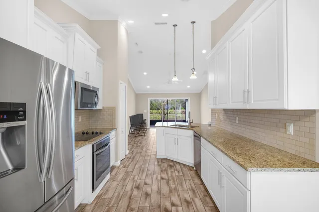 a kitchen with stainless steel appliances granite countertop a refrigerator a sink dishwasher a oven with white cabinets and wooden floor