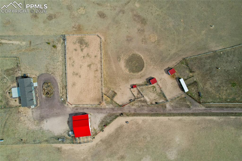 7880 J D Johnson Road Peyton, CO 80831 - Photo 23 of 50 Extensive rural property featuring a main residence with a gray roof, a large red barn, multiple smaller red outbuildings, a fenced arena, and a winding dirt driveway