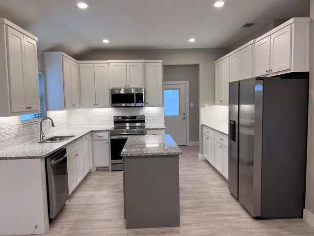 a kitchen with stainless steel appliances granite countertop a stove top oven a refrigerator and a sink