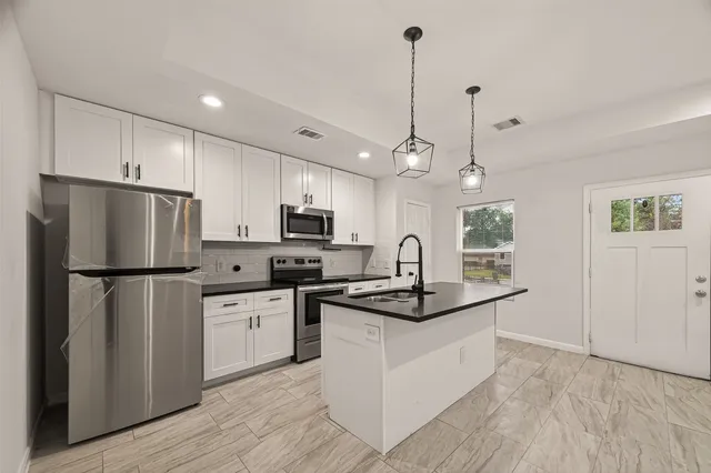 a kitchen with stainless steel appliances granite countertop a refrigerator a sink dishwasher a stove and white cabinets with wooden floor