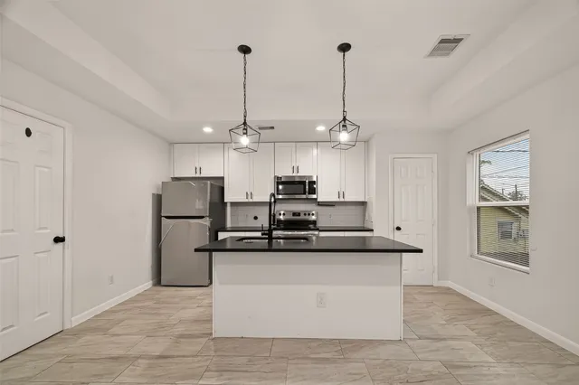 a view of a kitchen with stainless steel appliances granite countertop a sink a refrigerator and a chandelier
