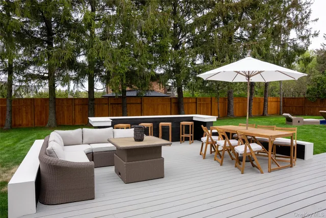 a view of a patio with couches and a table and chairs under an umbrella with wooden floor and fence