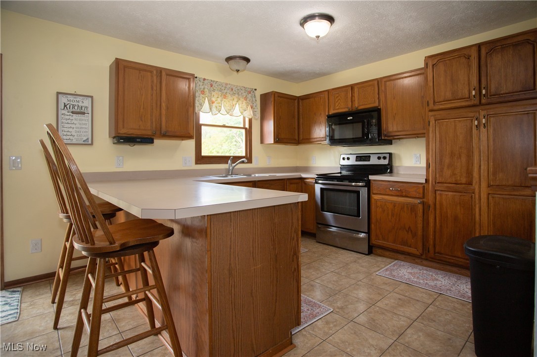4171 Laubert Road Atwater, OH 44201 - Photo 22 of 42 Kitchen with electric stove, sink, kitchen peninsula, light tile patterned floors, and a kitchen breakfast bar