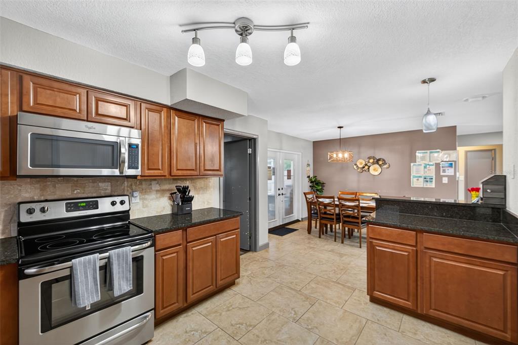 1576 Rosery Road Northeast Largo, FL 33756 - Photo 23 of 54 a kitchen with stainless steel appliances granite countertop a stove top oven a sink a dining table and chairs with wooden floor
