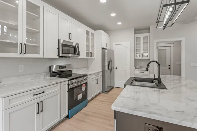 a kitchen with stainless steel appliances granite countertop a stove top oven a sink a refrigerator and white cabinets