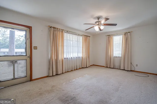 an empty room with chandelier fan and windows