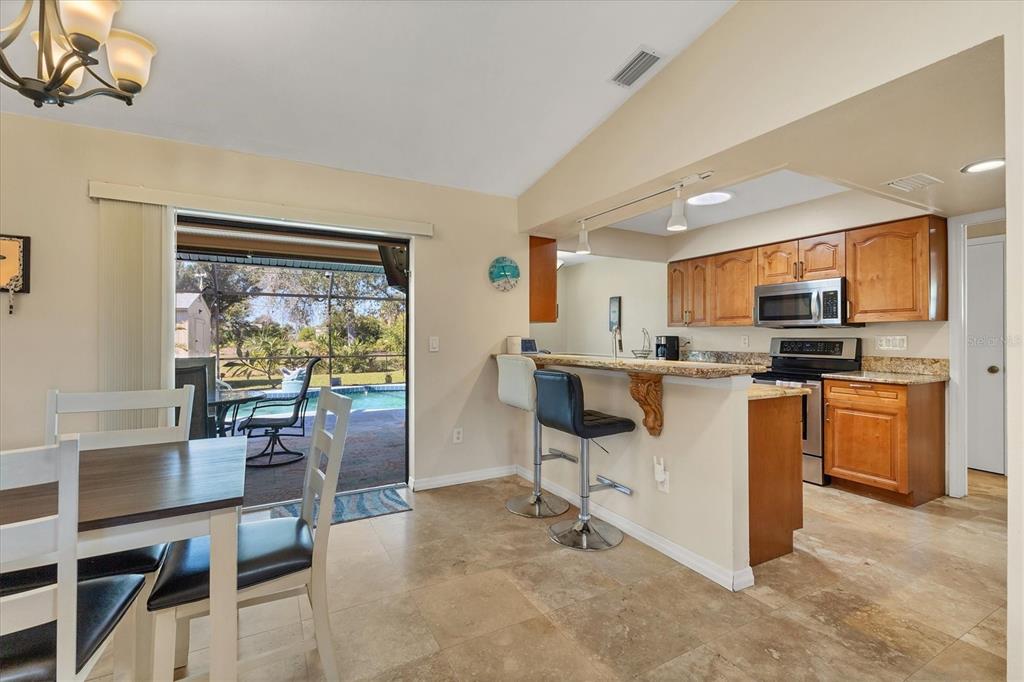 7047 Adderly Road Englewood, FL 34224 - Photo 8 of 39 a kitchen with stainless steel appliances kitchen island granite countertop a stove top oven a sink a dining table and chairs with wooden floor