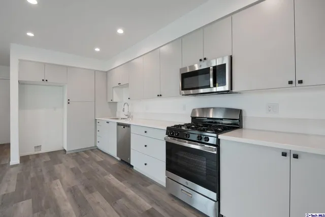 a view of empty room with wooden floor and kitchen view