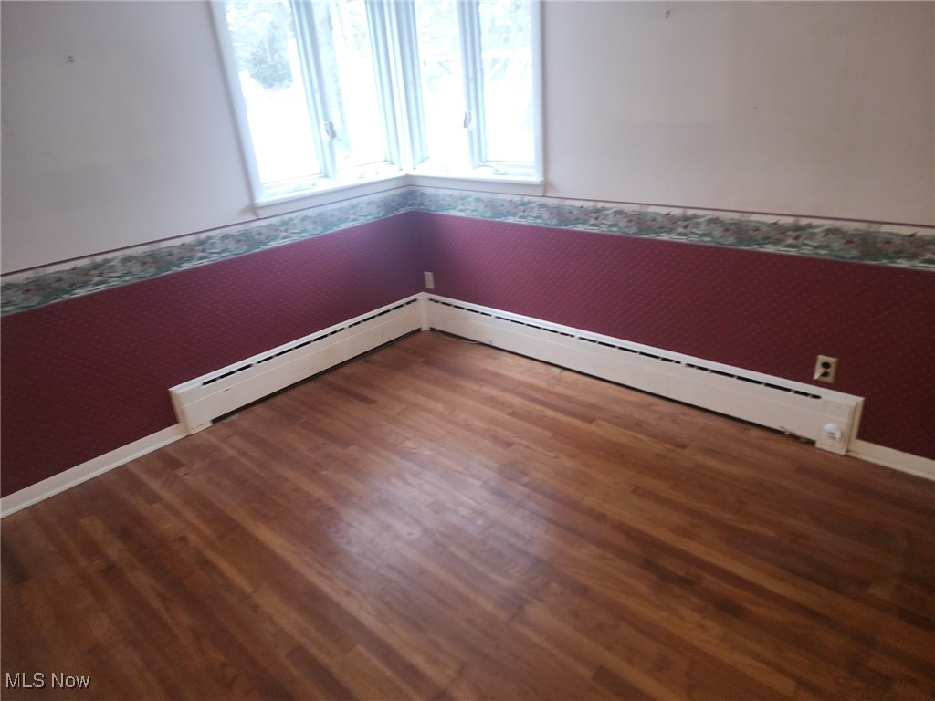 7516 Mayfield Road Chesterland, OH 44026 - Photo 13 of 21 Empty room with wallpapered walls, a baseboard radiator, and wood finished floors