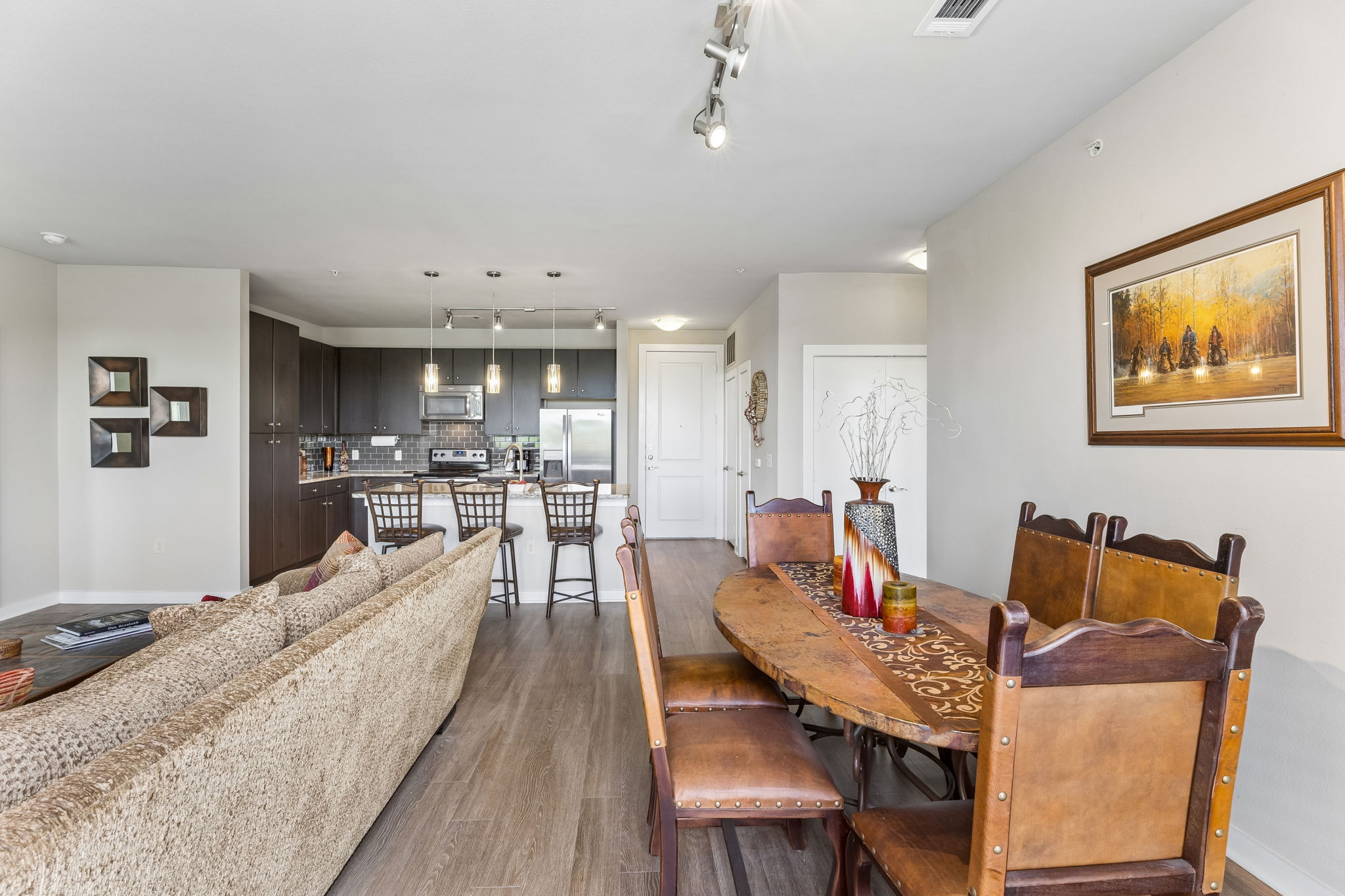 1900 Barton Springs Road, Unit 5032 Austin, TX 78704 - Photo 26 of 40 Open concept living area featuring wood-finish flooring, a kitchen with dark cabinetry, stainless steel appliances, a white island with pendant lighting, and a dining area