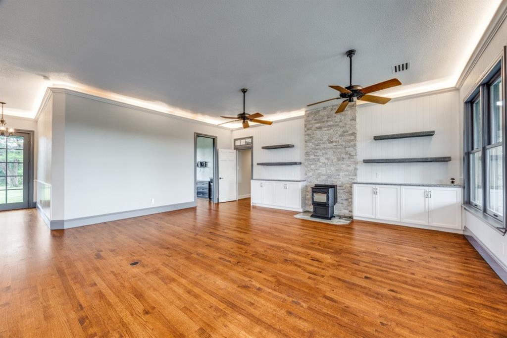 3244 Joe Davis Road Whitewright, TX 75491 - Photo 9 of 28 Unfurnished living room with a wood stove, ornamental molding, light wood-style floors, ceiling fan, and a chandelier