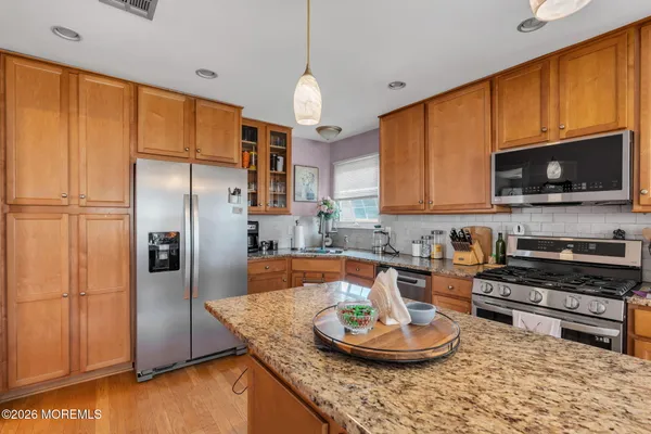 a kitchen with stainless steel appliances granite countertop a refrigerator a stove a sink dishwasher a dining table and chairs with wooden floor
