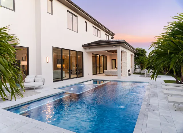 a view of a white house with a small yard plants and couches chairs