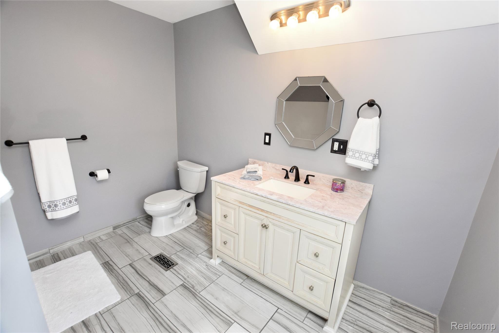 404 North Adelaide Street Fenton, MI 48430 - Photo 17 of 23 Modern bathroom featuring a white vanity with a light-toned countertop, an octagonal mirror, matte black fixtures, and gray-toned plank flooring