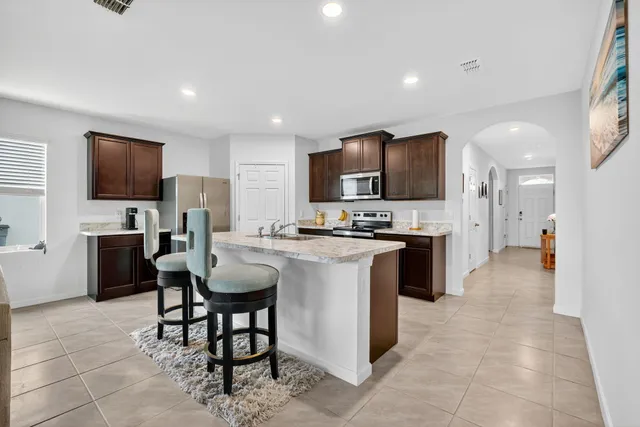 a kitchen with kitchen island granite countertop stainless steel appliances a refrigerator a stove a sink a dining table and chairs