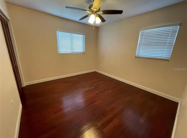 a view of an empty room with wooden floor and a chandelier fan