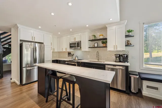 a kitchen with stainless steel appliances granite countertop a stove a sink a refrigerator and white cabinets with wooden floor