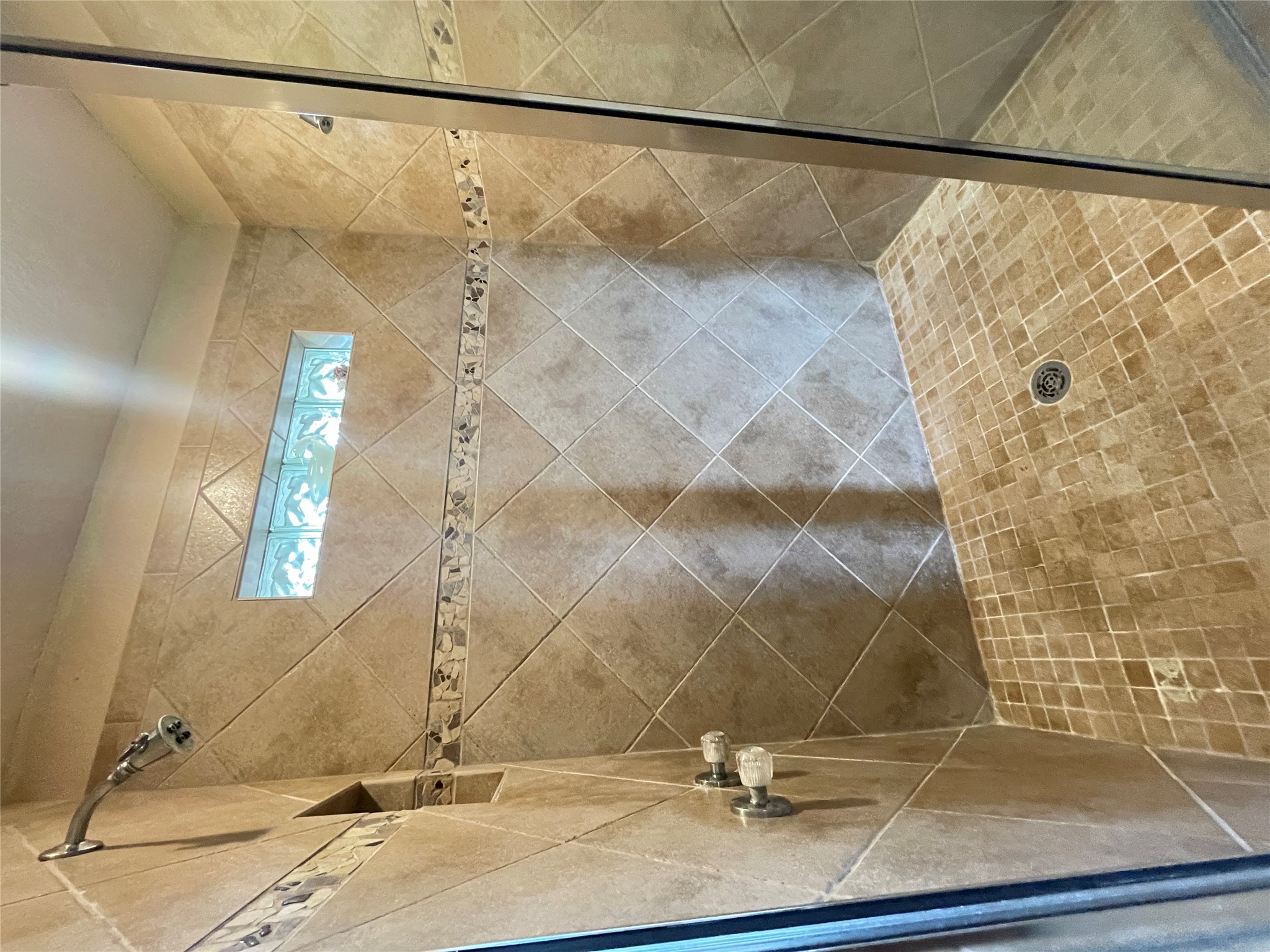 919 Little Ranches Road Wimberley, TX 78676 - Photo 11 of 13 A well-lit, tiled shower with a decorative border and a glass block window for natural light.