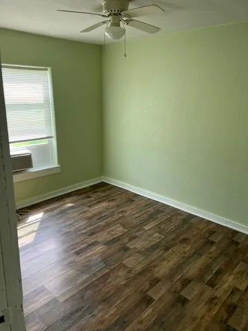 an empty room with wooden floor fan and windows