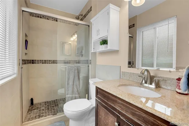 a bathroom with a granite countertop sink a toilet a mirror and shower