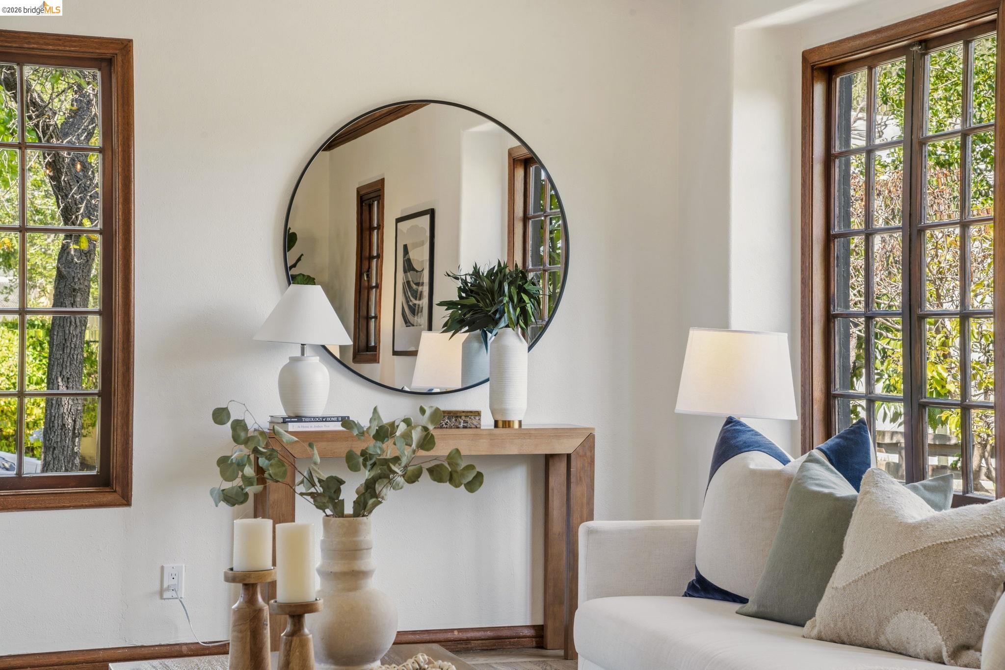 1087 Hubert Road Oakland, CA 94610 - Photo 48 of 67 Living area featuring a large round mirror, a console table with a wood-finish top, two windows with wood-frame muntins, and painted walls